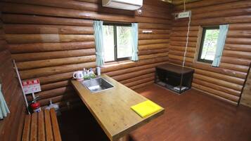 A log cabin with a wooden interior, a kitchen area with a sink and a stove, and two windows with curtains.