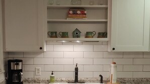 Una cocina con armarios blancos, encimera de granito, cafetera y lavamanos.