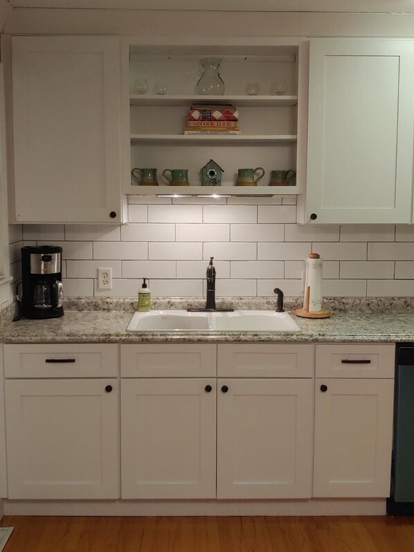 A kitchen with white cabinets, a granite countertop, a coffee maker, and a sink.