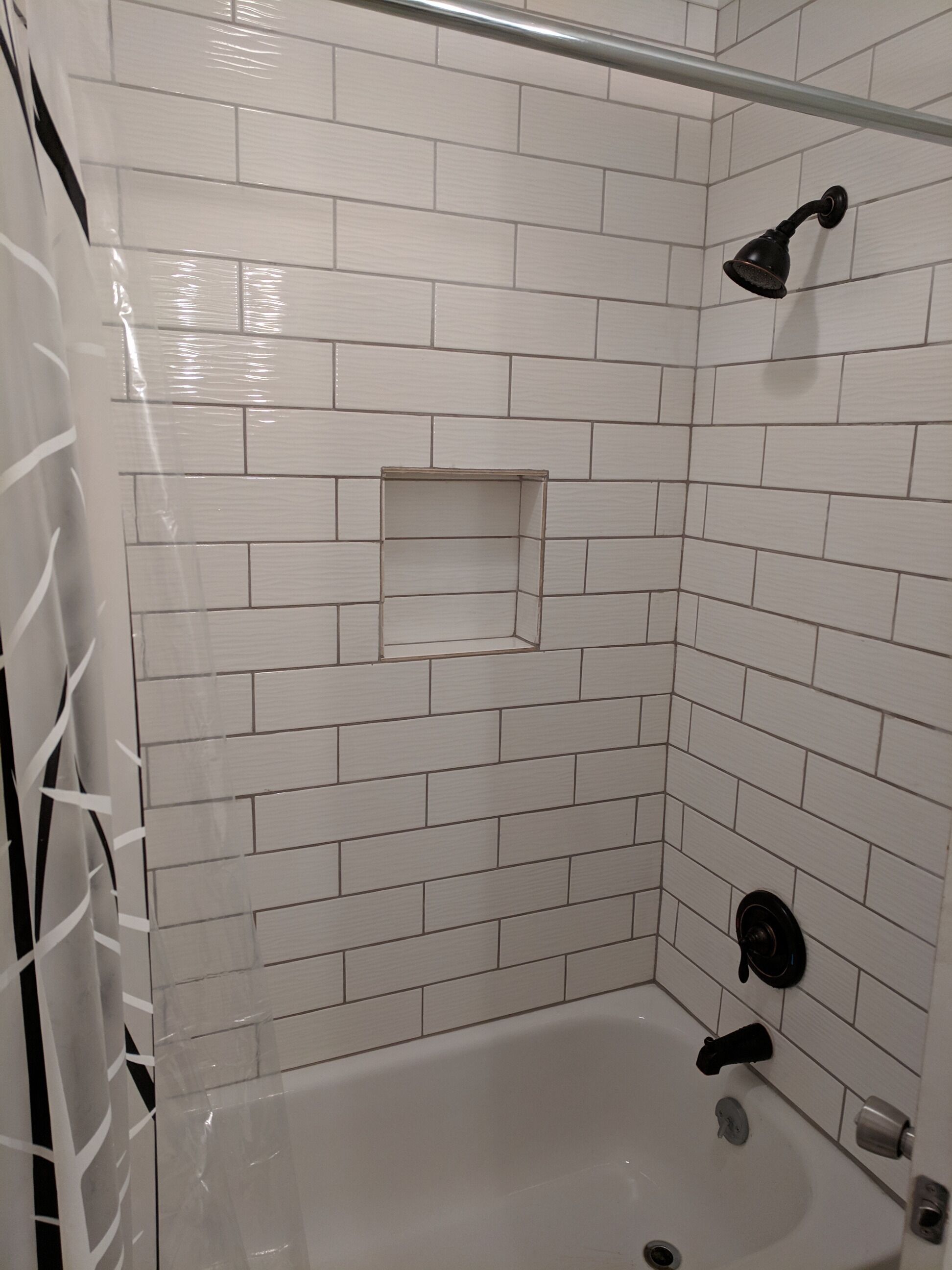 A shower area with white tiled walls, a glass shower enclosure, and a bathtub.