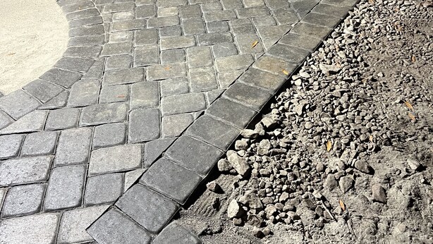 Una zona pavimentada con adoquines y grava, delimitada por una valla metálica y una estructura de madera.
