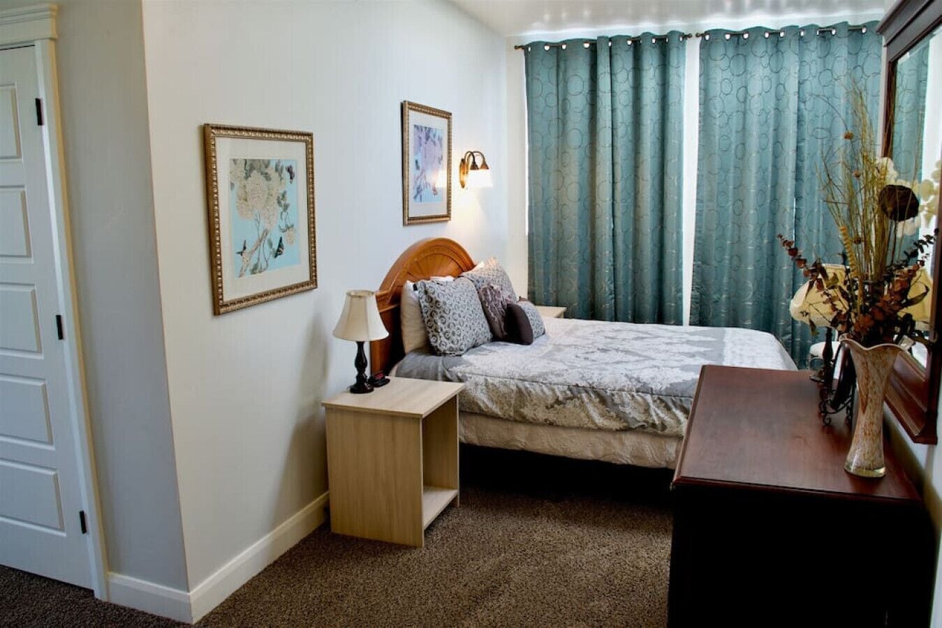 Ein ordentlich eingerichtetes Schlafzimmer mit Bett, Nachttisch, Lampe und einer Vase mit Trockenblumen.