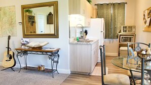 A compact living space with a kitchenette, a dining area with a glass table, a guitar, and a mirror. - LV5 Upper Floor Suite (La Verkin)