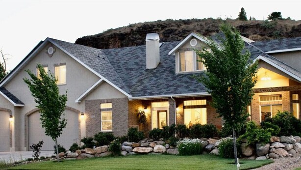 A two-story house with a stone facade, a sloped roof, and a well-maintained front yard with a lawn and a small tree. - LV5 Upper Floor Suite (La Verkin)