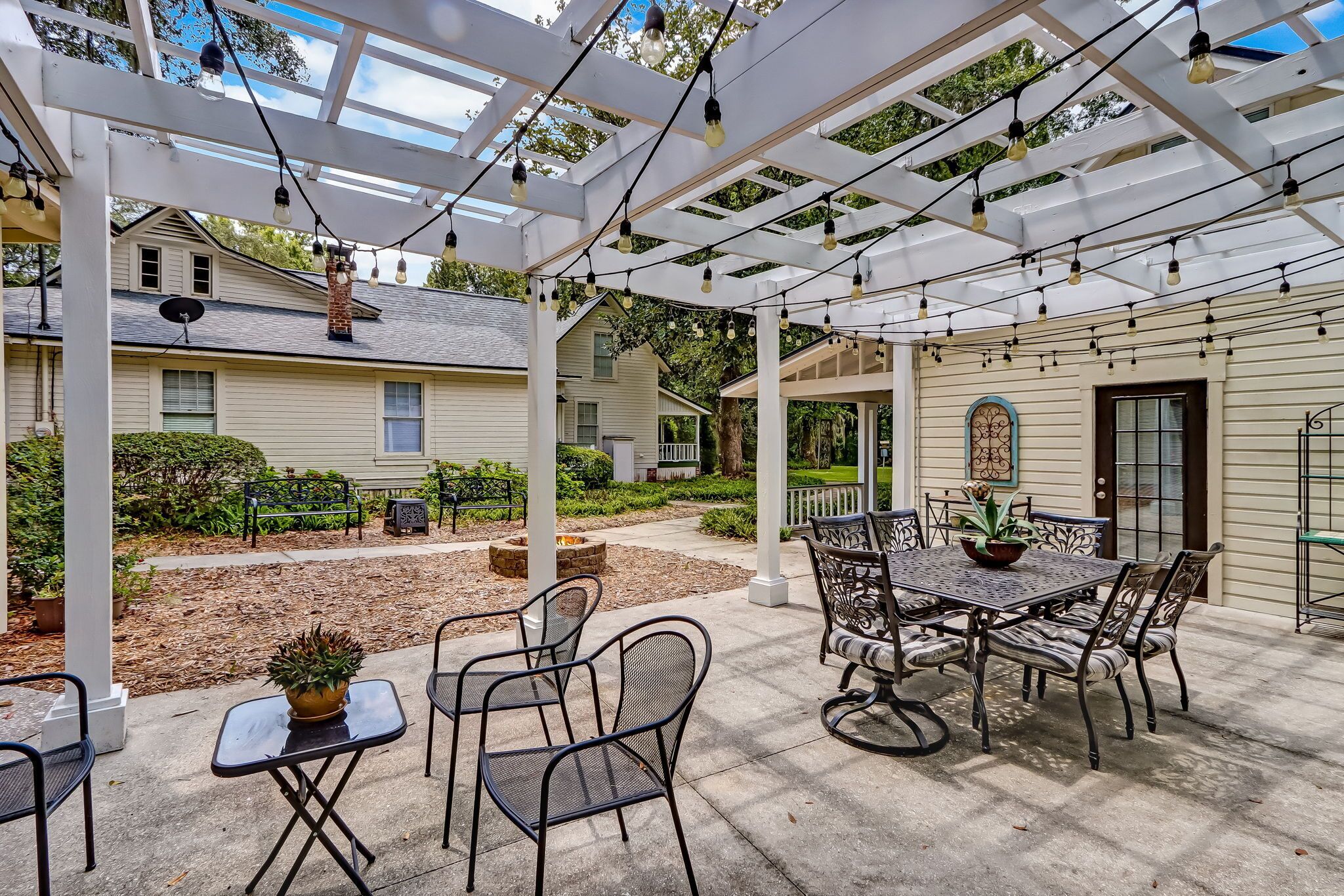 An outdoor patio with a pergola, string lights, and a dining table with chairs.