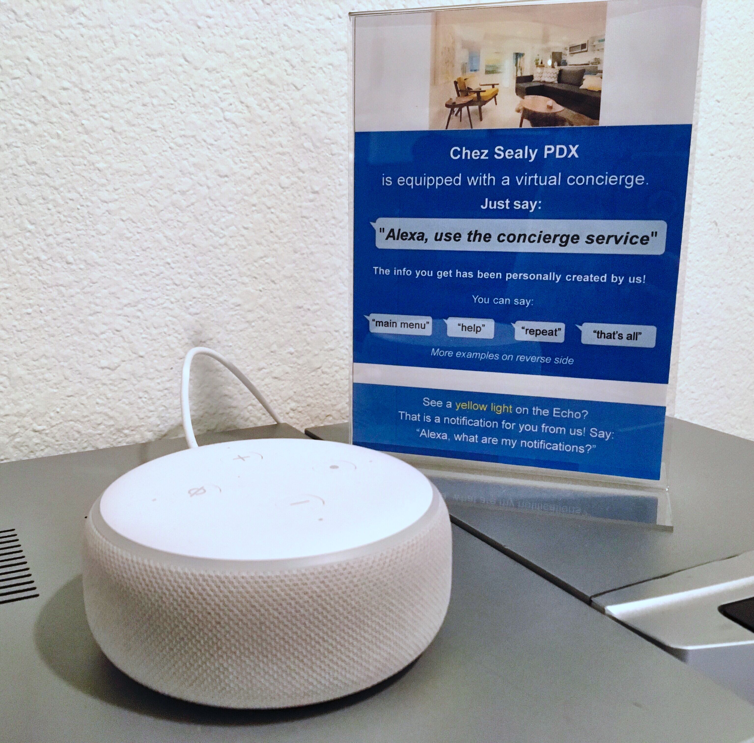 A white speaker device on a table with a sign about a virtual concierge service.