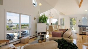 Amplia sala de estar con ventanas grandes, ventilador de techo y vista al mar.