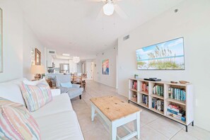 A spacious living room with a white sofa, a wooden coffee table, and a bookshelf filled with books.