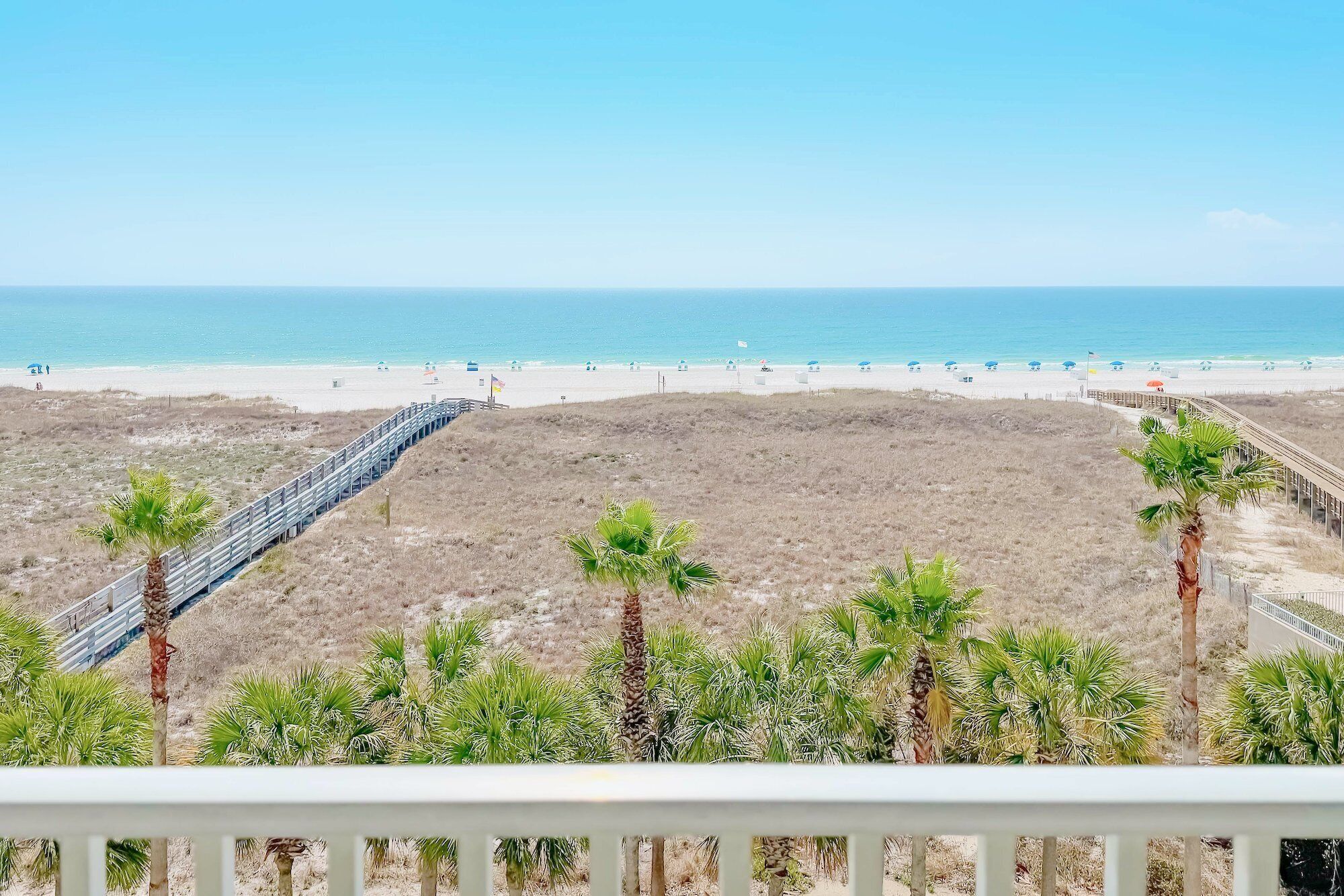 A beach with a wooden boardwalk leading to the shore, palm trees, and a clear view of the ocean.