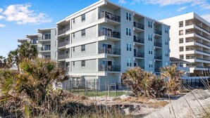 Un edificio residencial de varios pisos con balcones, suelo arenoso y palmeras.