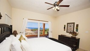 Ein Schlafzimmer mit Bett, Deckenventilator, Kommode und Fenster mit Ausblick ins Freie.