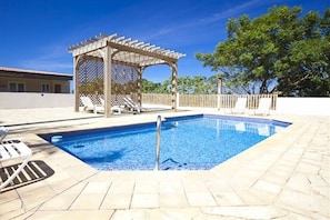 Une piscine rectangulaire agréée d’une pergola et de chaises longues, entourée d’une terrasse carrelée.