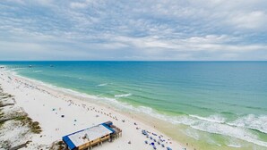 A beach with a pier extending into the ocean, a lifeguard station, and beach umbrellas.