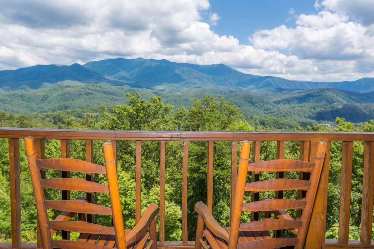 A wooden deck with two chairs facing a mountainous landscape.