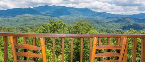 A wooden deck with two chairs facing a mountainous landscape.