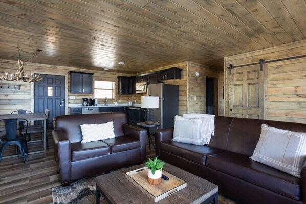 Interior de cabana com área de jantar, cozinha e dois sofás.