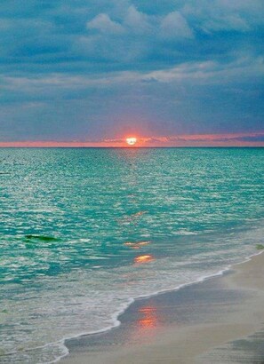 Une plage avec un coucher de soleil sur l’océan.