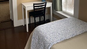 Un dormitorio con cama, escritorio con silla, lámpara, un cuadro y ventana con cortinas.