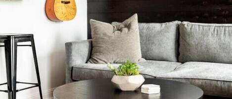 A modern living room with a grey sofa, a round black coffee table, and a guitar on the wall.