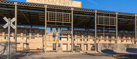 A large, industrial-style building with a sign reading "RIVERFRONT condominiums." It features a covered entrance with multiple levels and a metal framework.