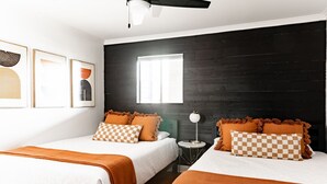 Een hotelkamer met twee bedden, een zwarte houten accentmuur, een raam en kunstwerken in lijsten aan de muur.