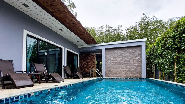 A modern outdoor swimming pool with lounge chairs and a stone wall. - Ton Yaang Private Pool Villa (Krabi)