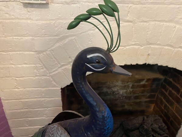 A peacock statue with a brick fireplace in the background.