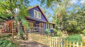 A two-story wooden house with a porch, surrounded by a wooden fence and greenery. - CLOSE TO DOWNTOWN- The Peacock Retreat- Dogs Stay Free  (Asheville)