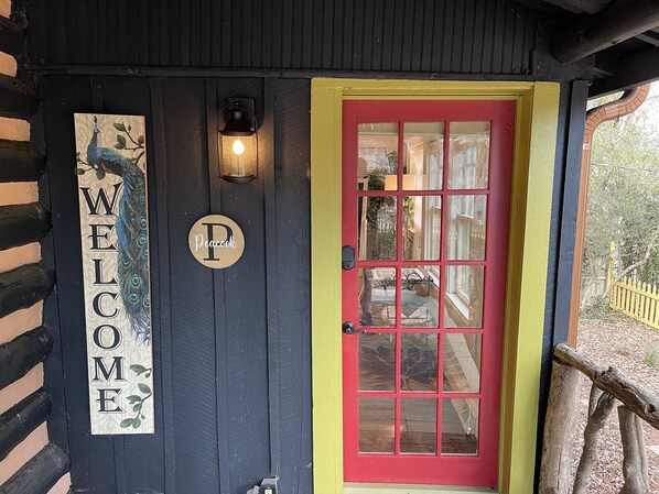 A black door with a red frame and a 'WELCOME' sign featuring a peacock.