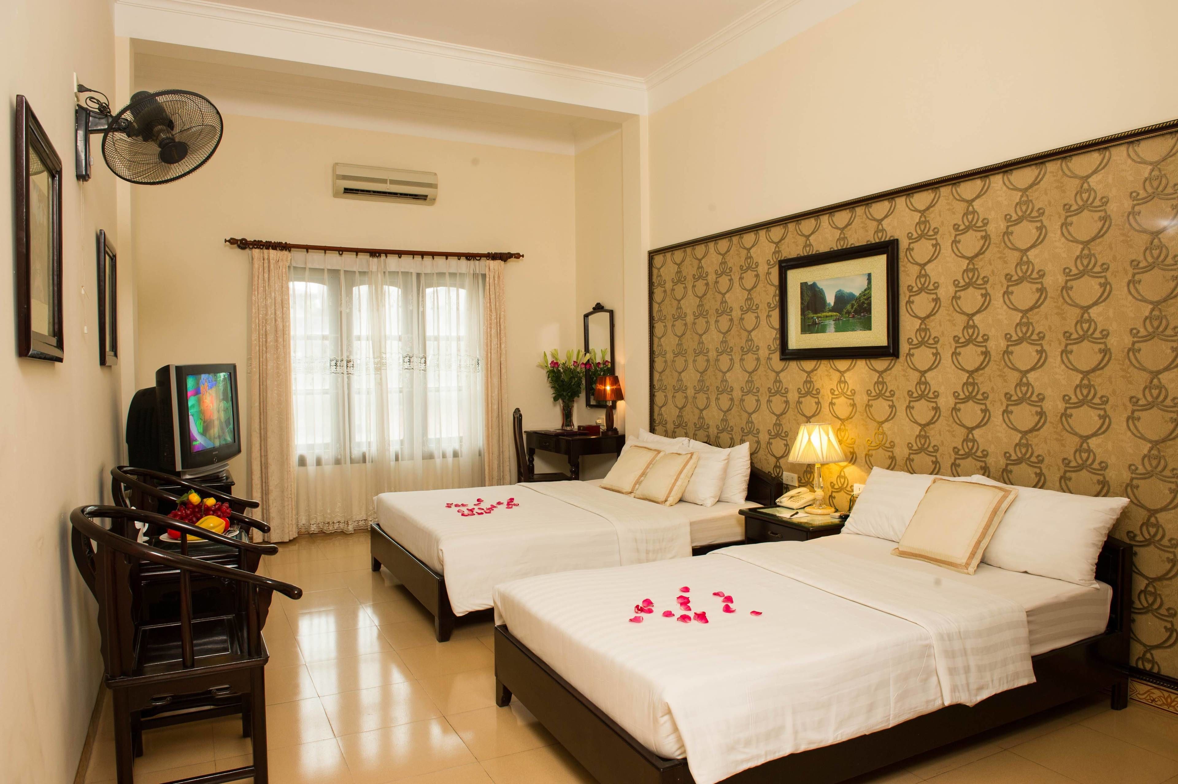 A hotel room with two beds, a TV, a fan, and a nightstand with a lamp.