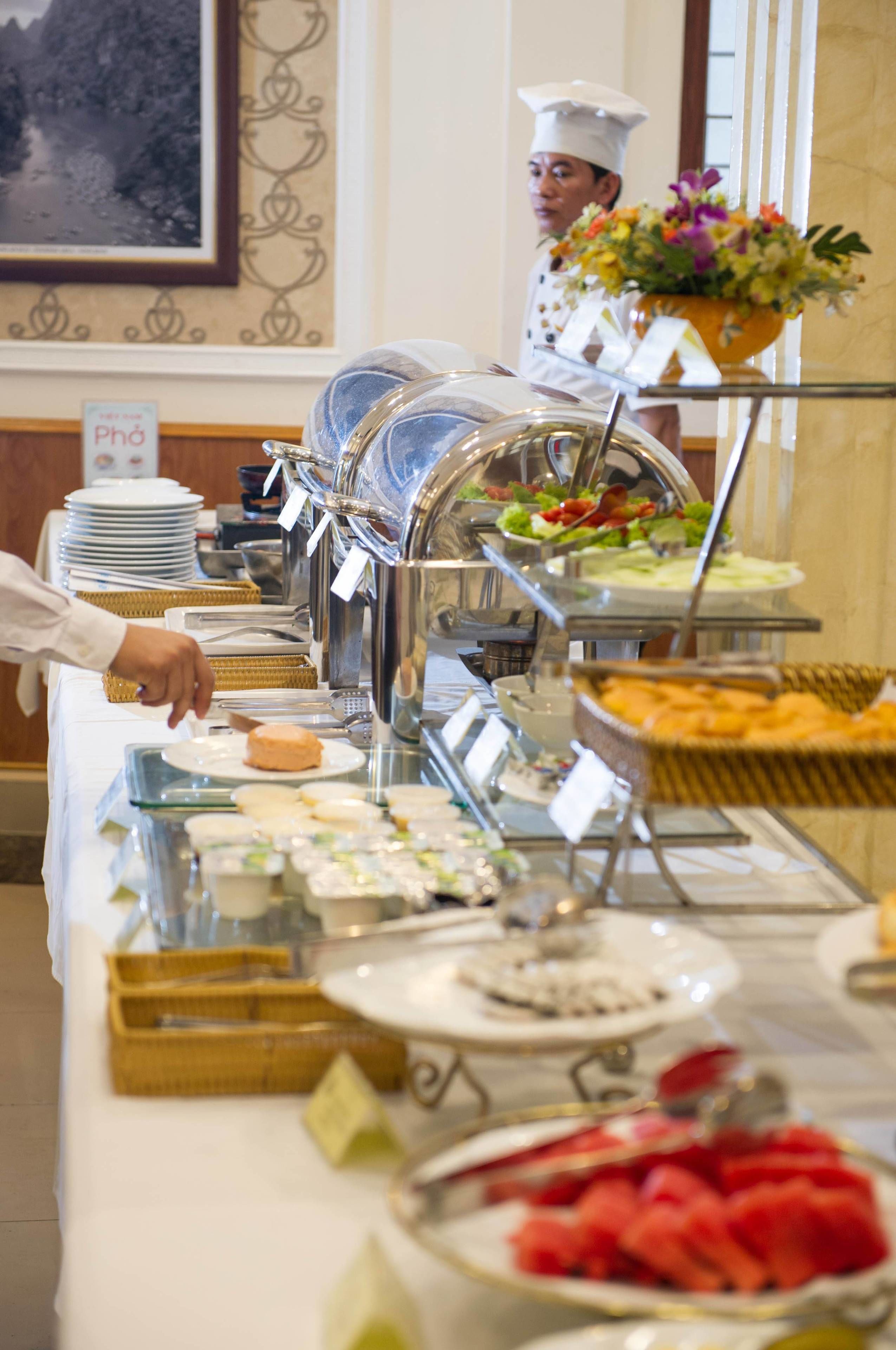 A buffet setup with various food items and a chef in the background.