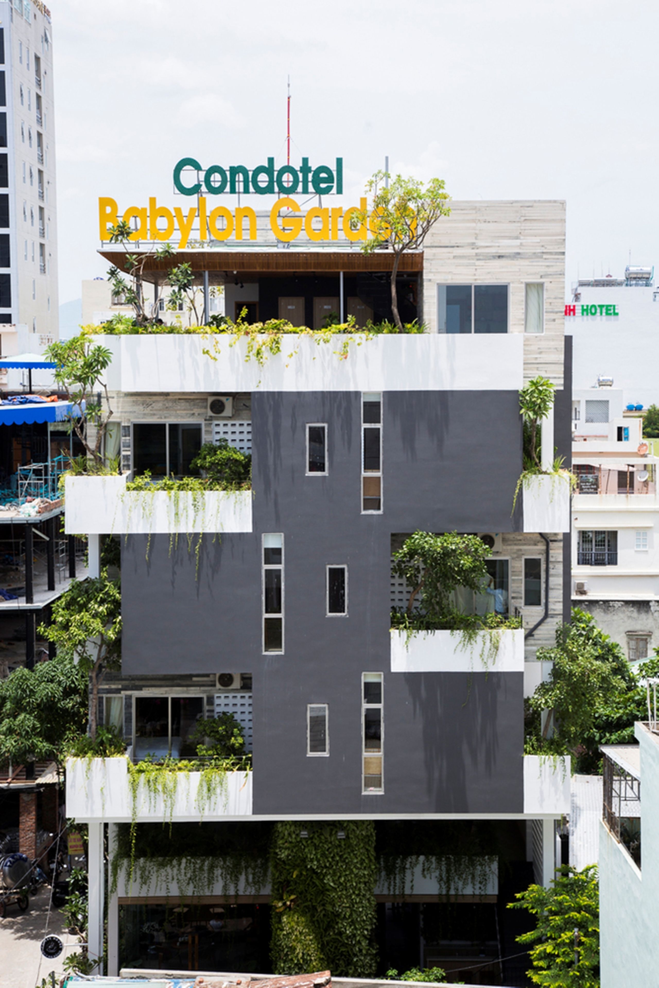 Ein mehrstöckiges Gebäude mit Balkonen, einem Schild mit der Aufschrift 'Condotel Babylon Gardens' und einem sichtbaren Hotelschild im Hintergrund.