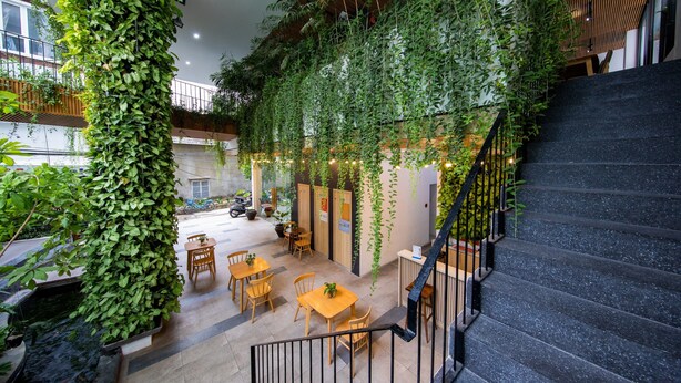 A spacious indoor area with a staircase, wooden tables, chairs, and a hanging garden. - Babylon Garden Condotel (Da Nang)