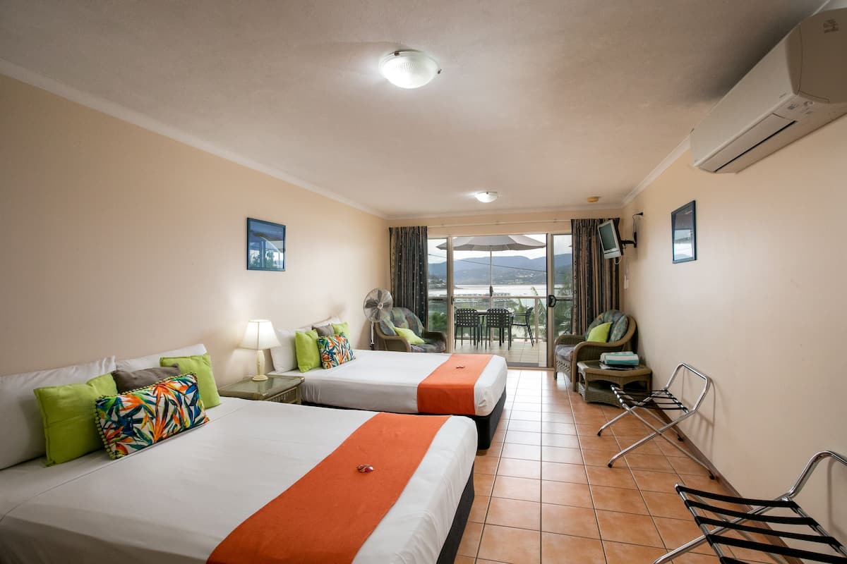 A hotel room with two beds, a balcony with a view, and a chair.