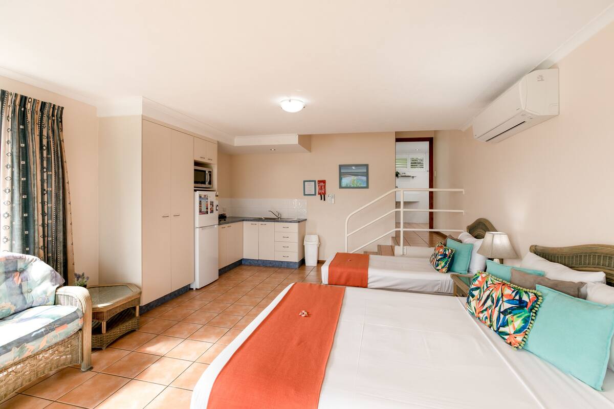 A hotel room with a bed, a sofa, a small kitchen area, and a staircase.