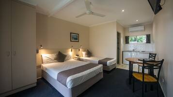 A hotel room with two beds, a desk, and a chair. There is a ceiling fan, a window with curtains, and an air conditioning unit.