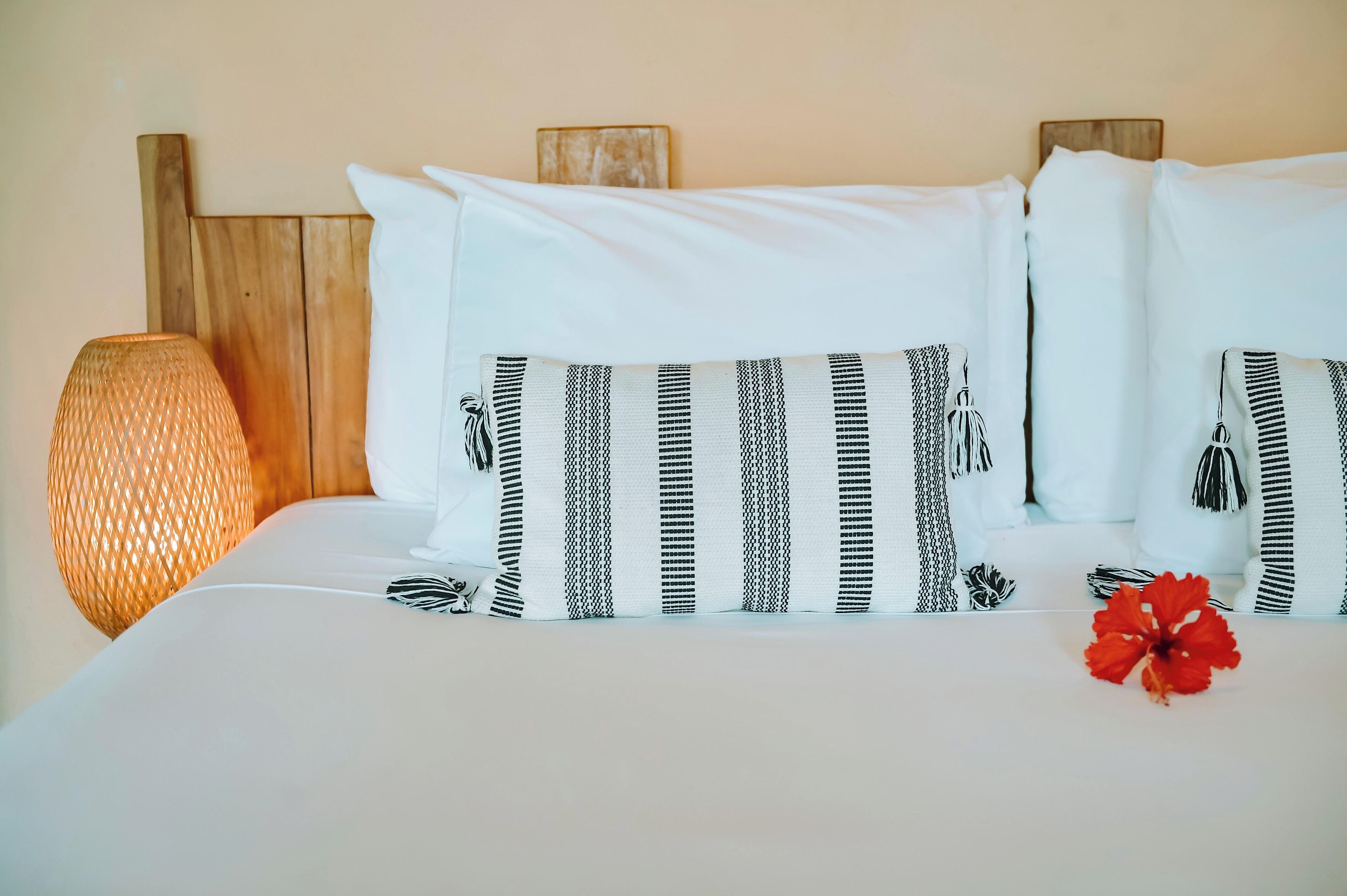 A neatly made bed with white bedding and striped pillows, a wooden headboard, and a textured lamp beside it.
