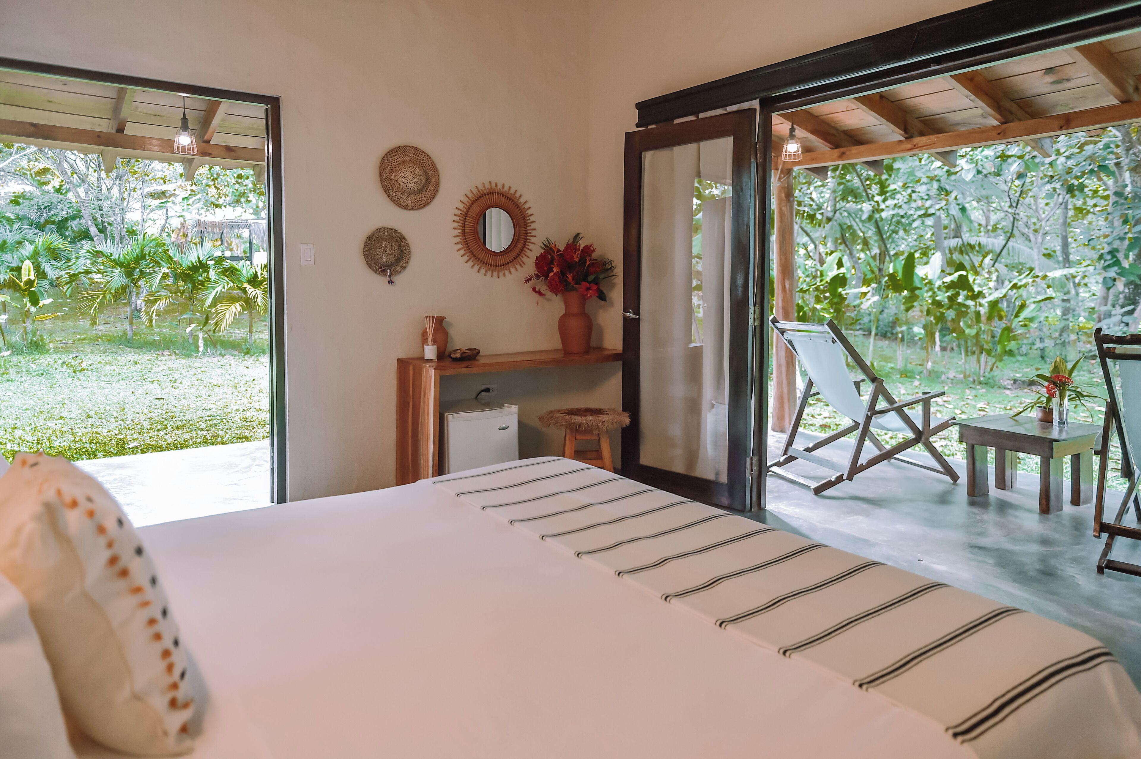 A bedroom with a bed, a small desk, a chair, and a view of a garden.