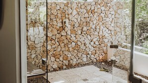 A stone wall with a rustic, natural look, a bench, and a glass door leading to an outdoor area with a tiled floor and greenery visible through the door. - Villa Coco (Hicaco)