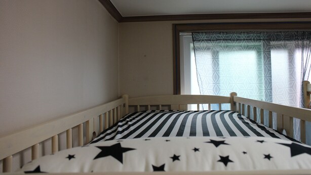 Una habitación con una cama, cubierta con un edredón estampado de estrellas, un cabecero de madera y una ventana con cortinas decoradas.