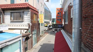 Una calle urbana estrecha con edificios, un toldo rojo y un poste de metal.