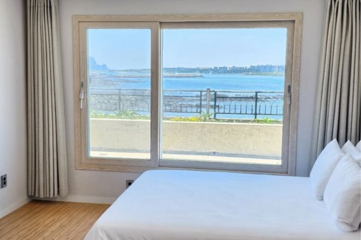 A hotel room with a large window, a bed, and curtains.