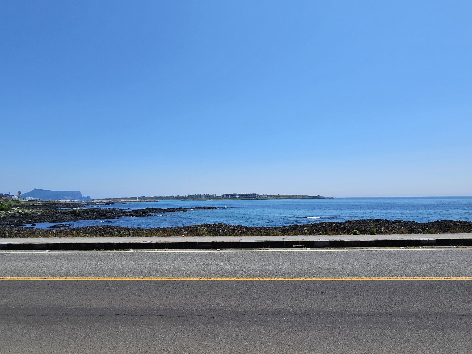 A coastal road with a clear view of the ocean and distant buildings.