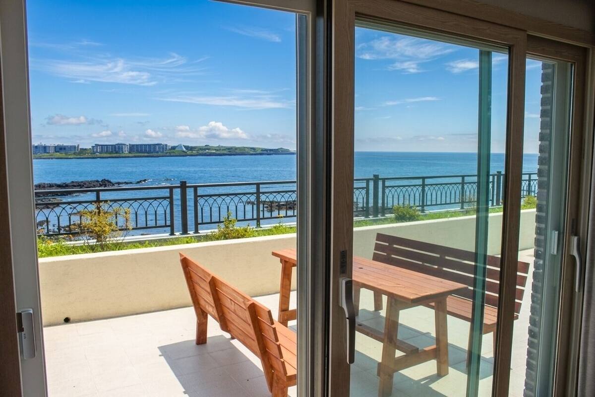 Un balcón con vistas al mar, bancos de madera y una mesa.