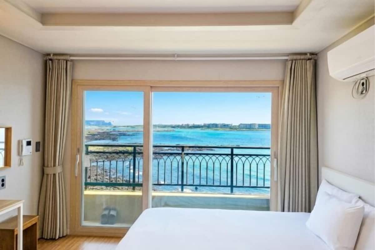 Habitación de hotel con una cama grande, vistas al mar y un balcón con cortinas.