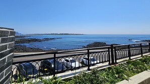 A coastal road with a black metal fence, parked cars, and a clear blue sky. - Haemorat (Seogwipo)
