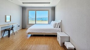 A hotel room with a bed, a desk, a chair, a bedside table, and a view of the sea. - Haemorat (Seogwipo)
