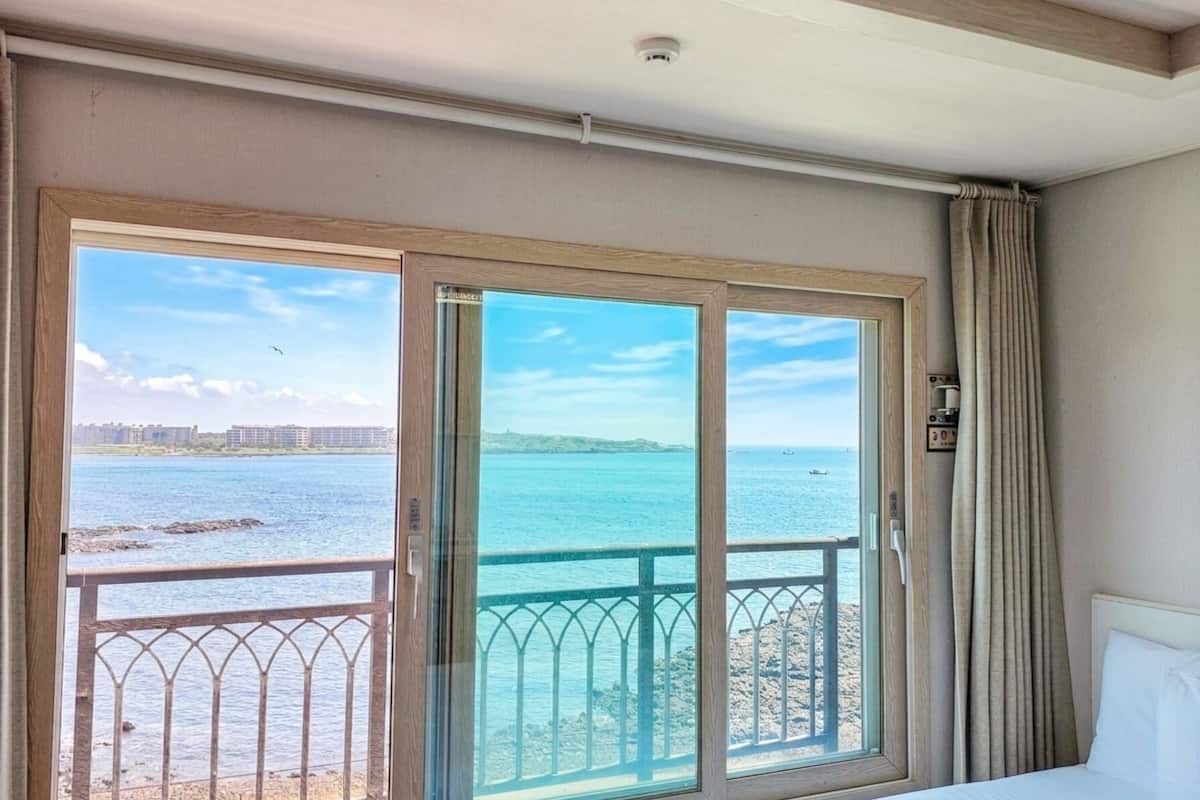 Habitación de hotel con un amplio ventanal corredero que da a un balcón con vistas al mar y edificios al fondo.
