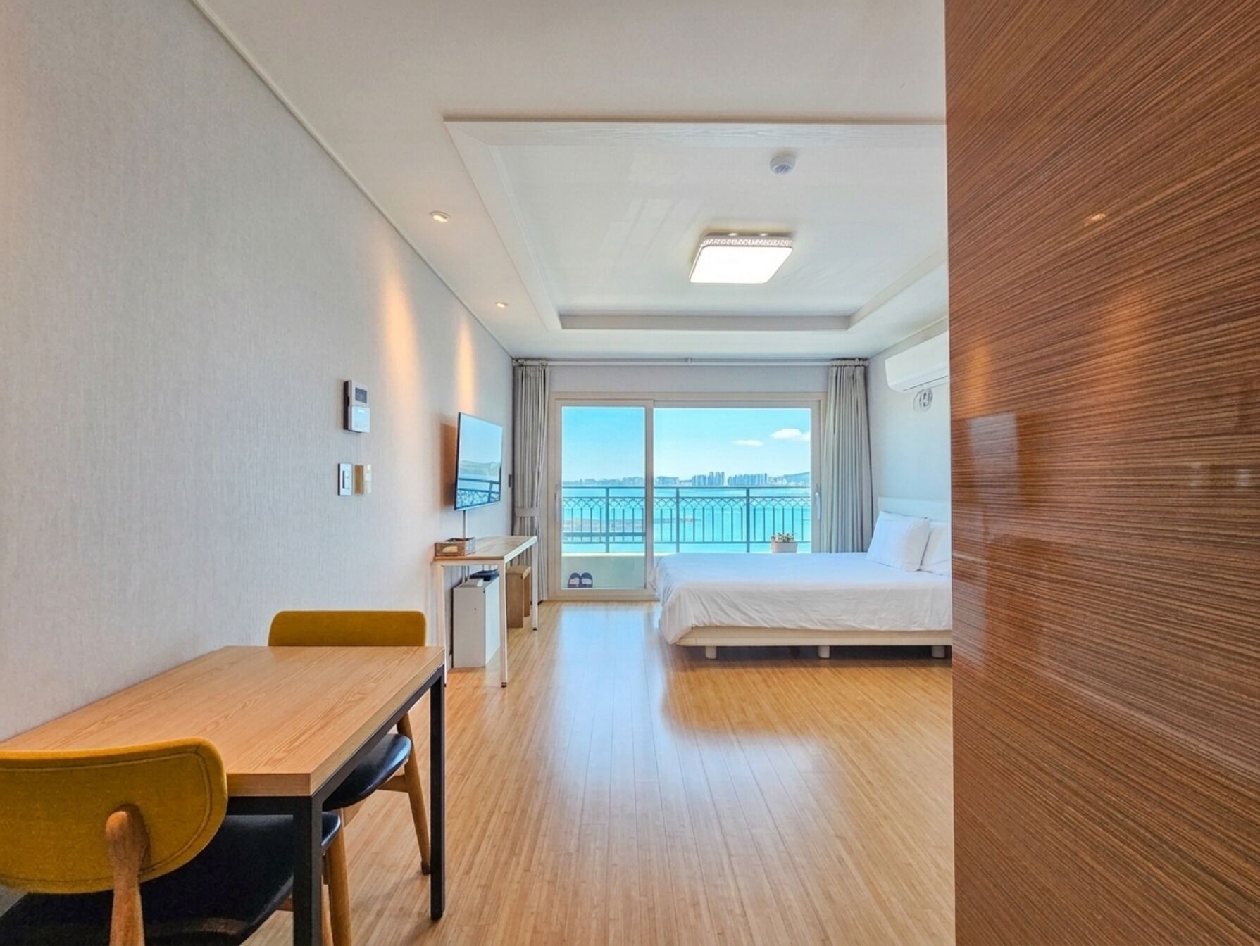 Habitación de hotel con cama, escritorio, silla, televisor y ventana grande con vistas.