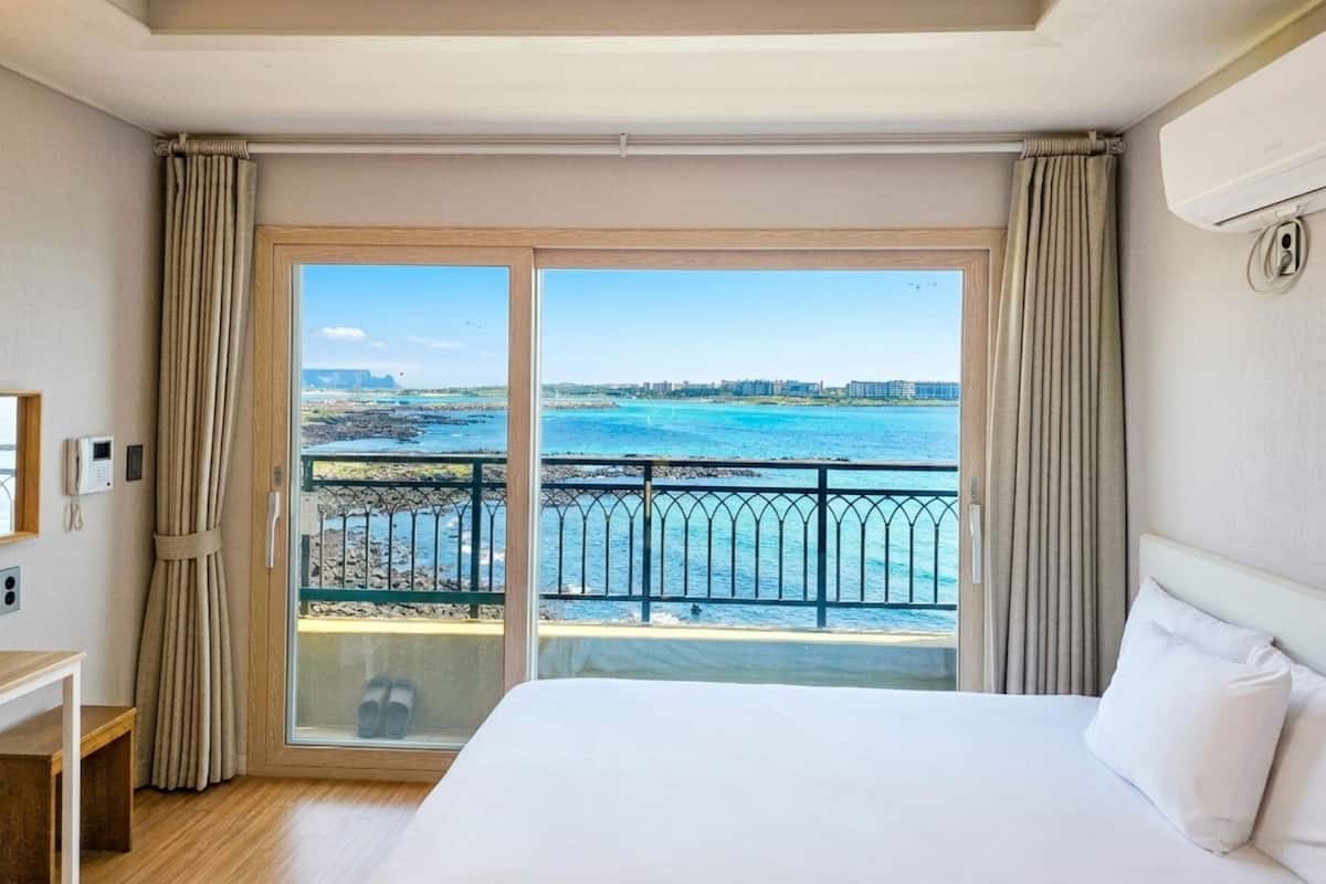 Habitación de hotel con una cama grande, vistas al mar y un balcón con barandilla.